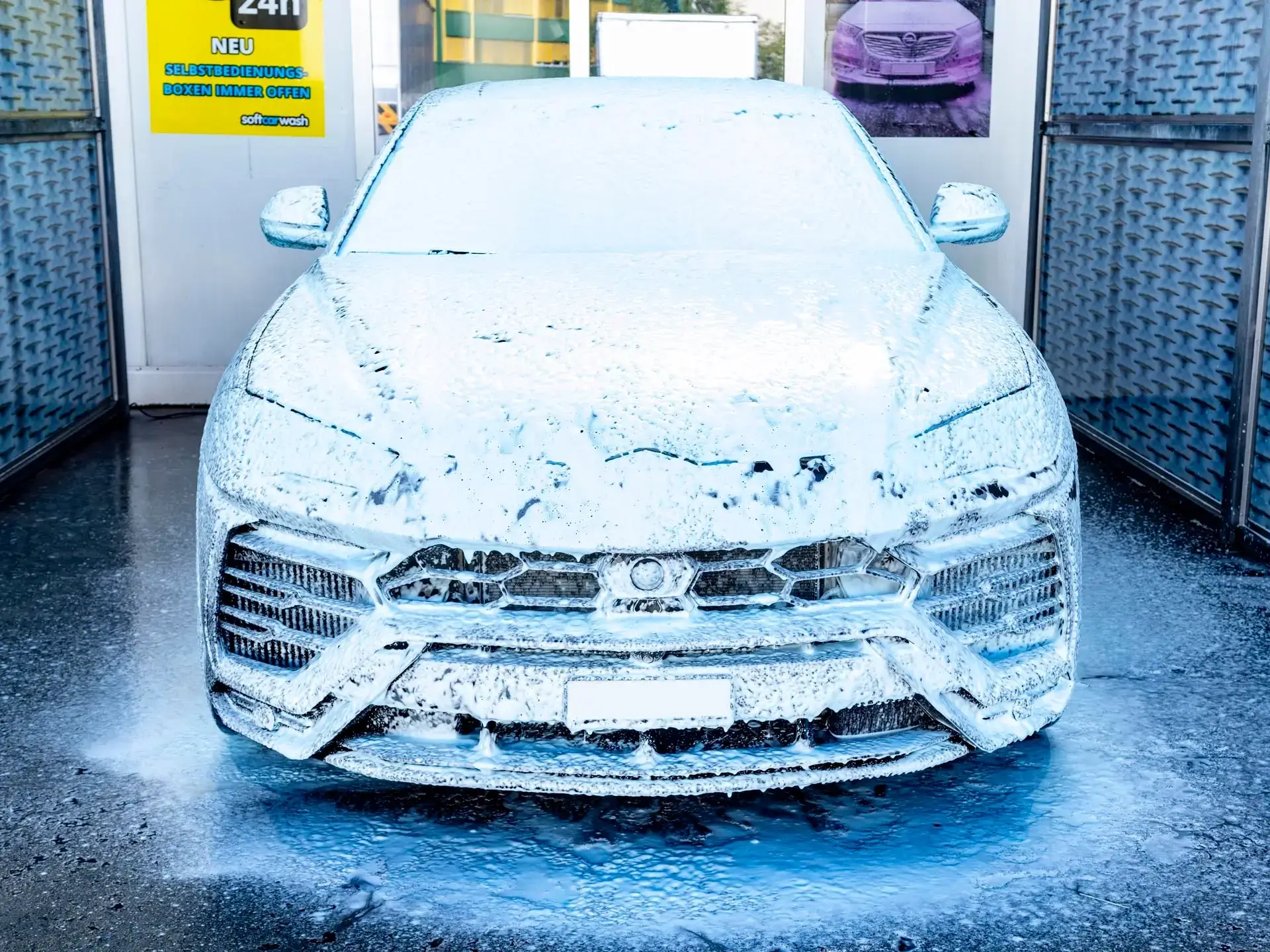 Ein Auto, das an einer Autowaschanlage mit dickem weißem Schaum bedeckt ist. Ein Auto, das an einer Autowaschanlage mit dickem weißem Schaum bedeckt ist.