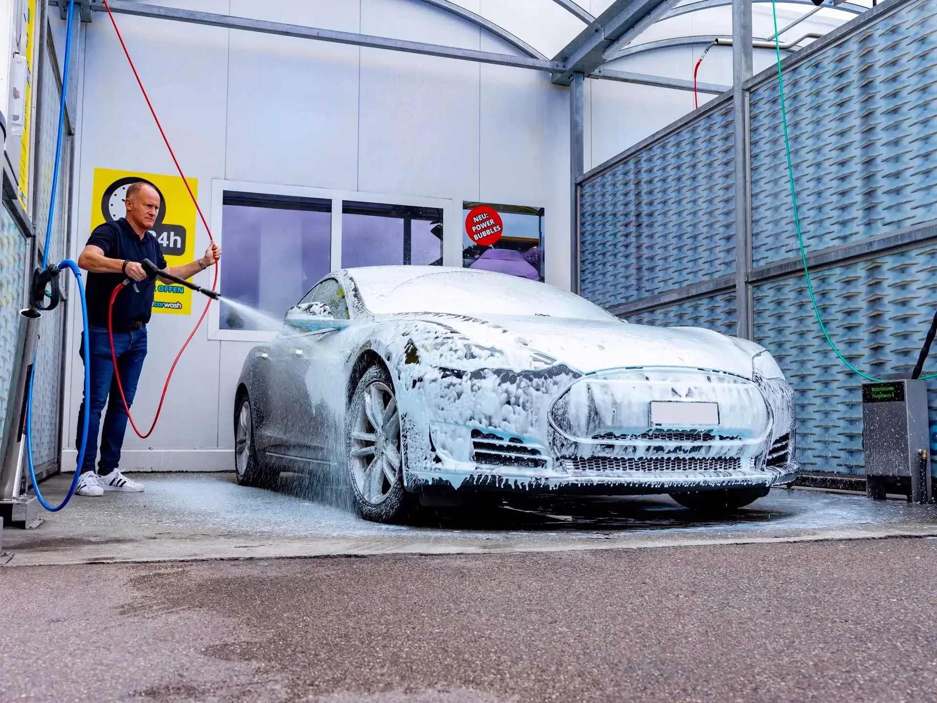 Eine Person, die an einer Selbstbedienungs-Autowaschanlage ein weißes, mit Seife bedecktes Auto wäscht.