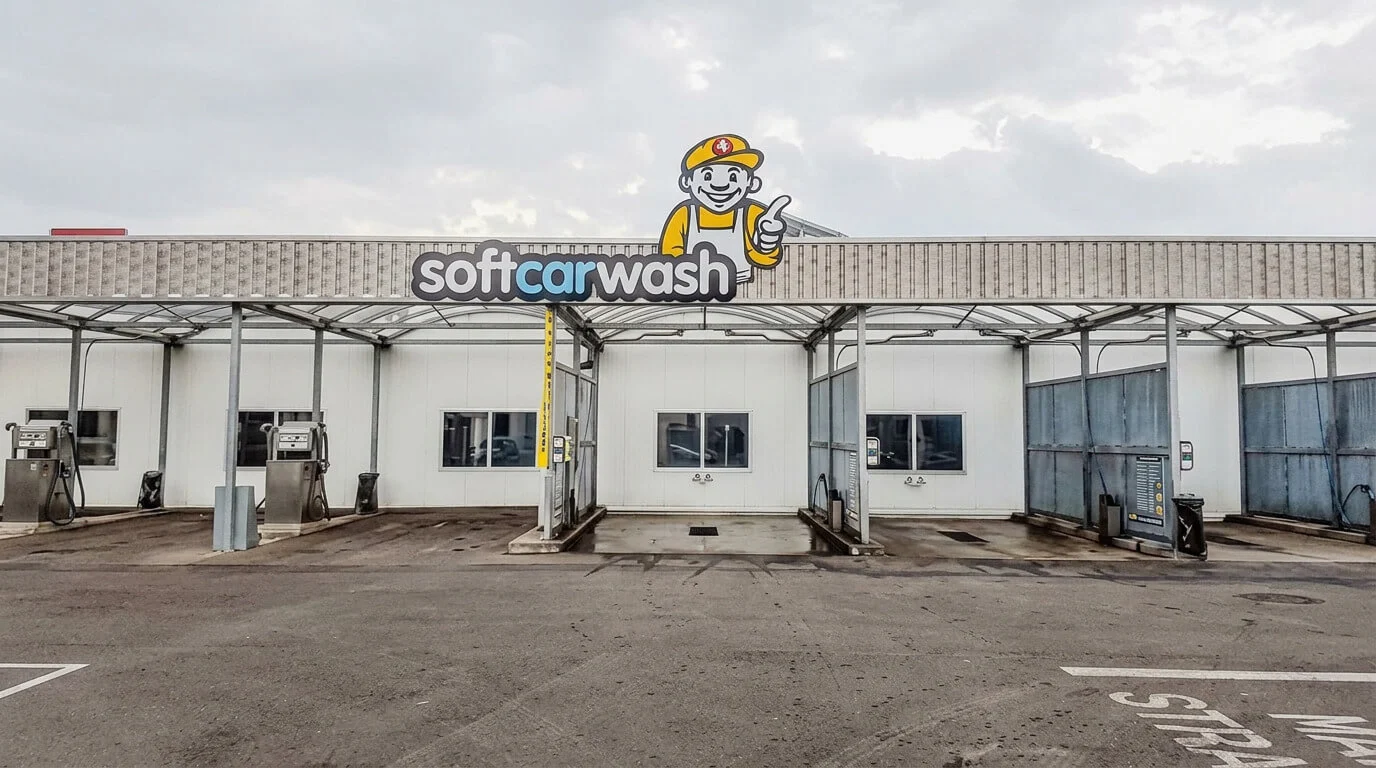 Leere Selbstbedienungs-Waschplätze mit einem „Soft Carwash“-Schild und einer Comicfigur darauf. Leere Selbstbedienungs-Waschplätze mit einem „Soft Carwash“-Schild und einer Comicfigur darauf.