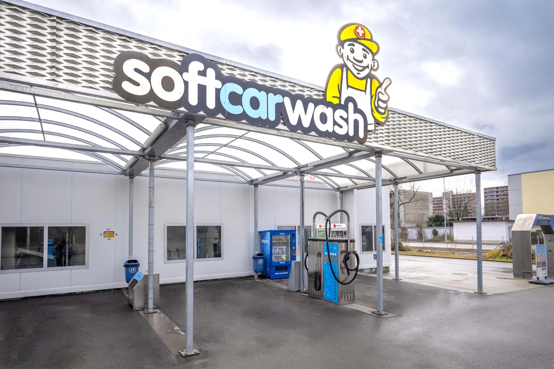 Soft-Autowaschanlage im Freien mit Cartoon-Maskottchen, blauen Maschinen und überdachtem Dach.